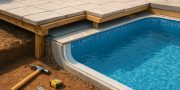 Close-up view of a partially constructed patio area adjacent to a pool, with tools like a hammer and measuring tape visi